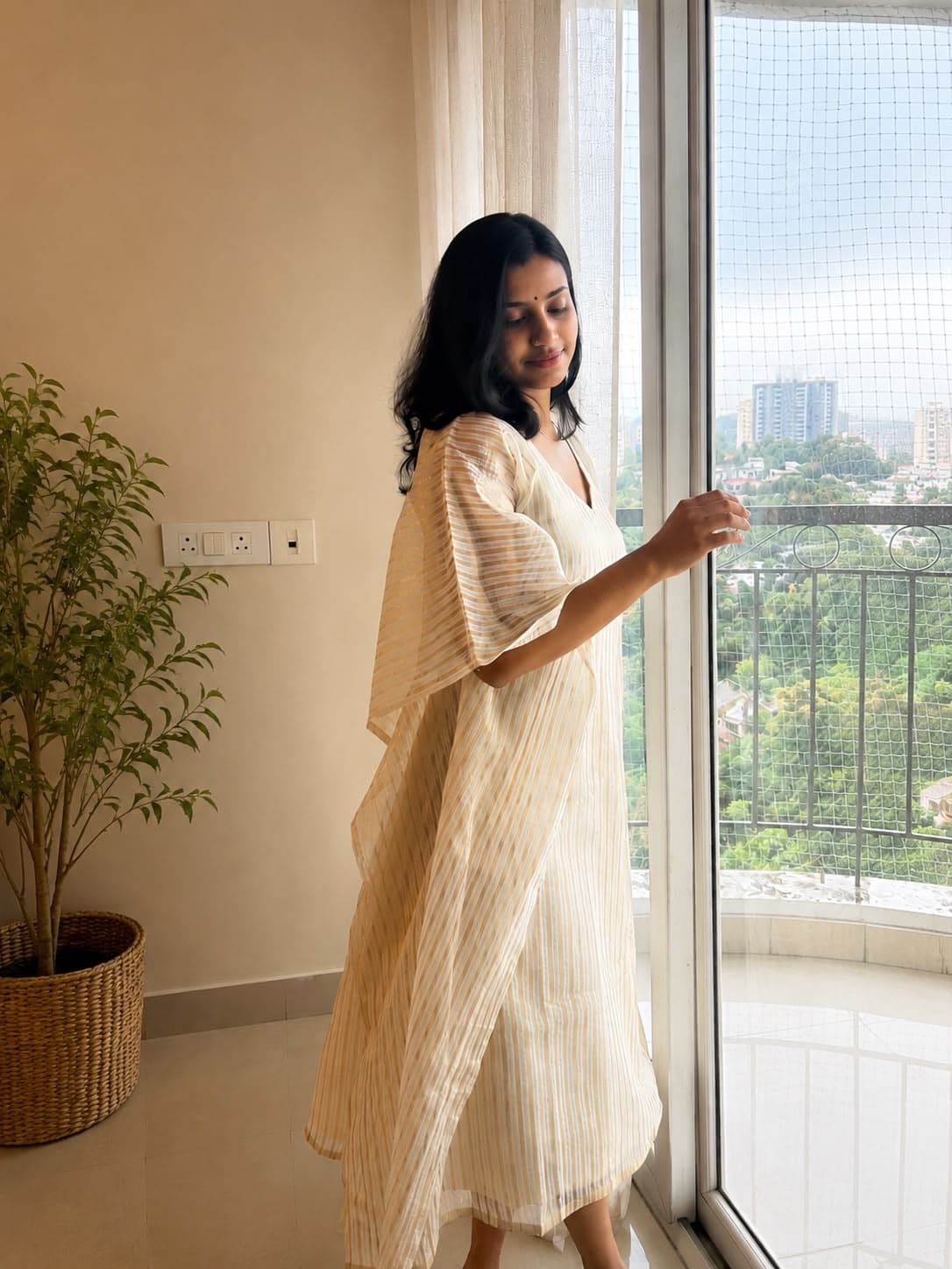 The Ponnila Kaftan in ivory and gold, worn against soft window light